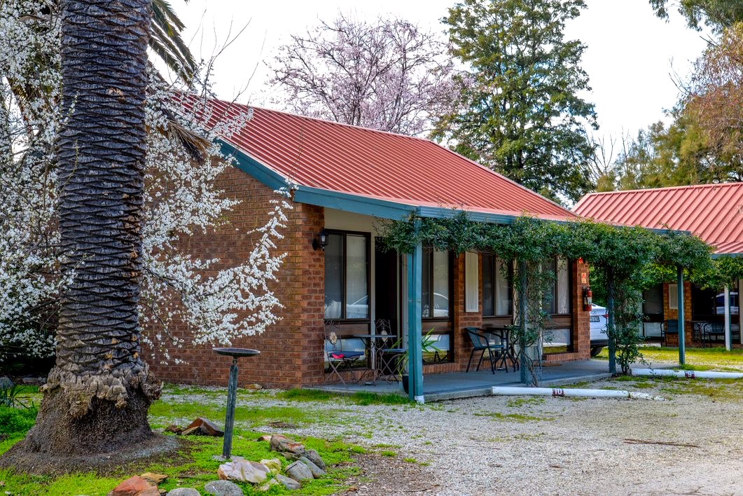 Rooms 9 and 10 at Jolly Swagman Motor Inn — brick unit with a red roof beneath a blossoming tree